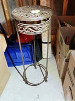 Full view of the cast iron plant stand with curved legs and decorative round top, seen among storage items