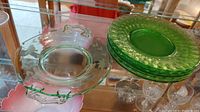 Stacked 5 green uranium glass dessert plates and 1 larger serving plate, displayed in glass cabinet.