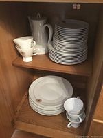 Overall view of stacked plates, cups, saucers and coffee pot inside cabinet