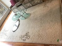 Full view of large white wool rug in living area. Shows embossed floral and vine designs with scattered pastel floral embroidery and fringe on one edge.
