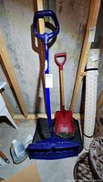 Full view of two snow shovels and metal pot on the floor, showing condition and overall appearance
