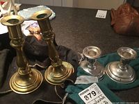 Two pairs of candlesticks shown together - one pair sterling silver around 3 inches tall, one pair brass around 8 inches tall.