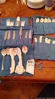 Four blue fabric roll-up pouches laid out on table showing assorted spoons, knives and spreaders