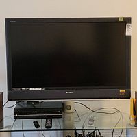 Front view of Sony Bravia TV on glass stand with remotes and device beneath