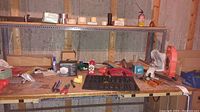 Wide shot of workbench with assorted hardware items including screwdrivers, clamps, tape, wires, small containers, and boxes.