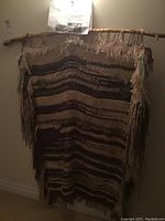 Full view of the large woven wall hanging on a beige wall, showing the whole piece hanging from a branch holder.