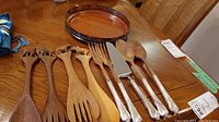 Photo showing wooden carved animal handle utensils, silver plated handled forks, spoons, and serving utensils, plus a wooden serving bowl.