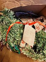 Small artificial Christmas tree with green faux pine branches and beige fabric ribbon decorations inside a box.