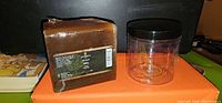 Photo of brown soap base block with label and clear plastic jar with black lid on orange surface.