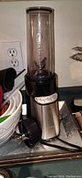 Cuisinart blender base in stainless steel and black plastic with a tall blending cup attached on top, showing the control buttons on the front and power cord at the base.