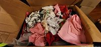 Box containing assorted fabric pieces including lace trims and solid-colored fabric in pink, red, and white tones.