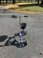 Front view of a blue knee scooter with black knee pad and handlebars on pavement outdoors.
