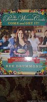 Front cover of The Pioneer Woman Cooks: Come and Get It cookbook by Ree Drummond, showing the author holding a dish with a colorful floral border.