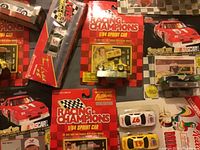 Photo showing multiple Racing Champions NASCAR and Sprint Car die-cast cars in original packaging, mostly red themed with cars numbered 51 and 5 visible