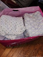Photo showing sheets folded inside a pink storage container, including white with dots and lavender geometric patterns