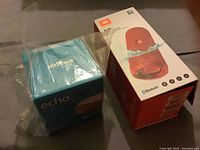 Photo showing the Amazon Echo in blue box and JBL FLIP 4 red speaker box side-by-side, both new and boxed.