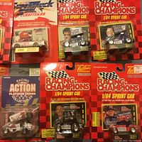 Photo showing multiple 1/64 sprint cars and Super Truck diecast models in blister packaging with Racing Champions branding and driver photos.