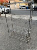 Full view of adjustable chrome four-shelf wire rack outdoors on pavement, showing structure and condition.