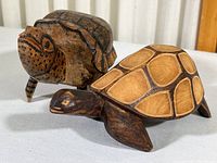 Two carved wooden turtles, one with an upright shell and detailed etchings, the other with an elongated shell and geometric patterns.
