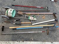 Full view of all garden tools laid out on asphalt showing variety including powered edger, shovels, hoes, hand pruners, and rakes.