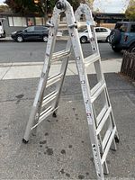 Full view of Gorilla Ladders adjustable aluminum ladder in A-frame position outdoors on pavement.