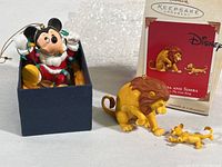 Mickey Mouse ornament in Santa outfit inside blue box next to Mufasa and Simba Lion King ornament with original packaging in background