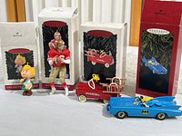 Four Hallmark Keepsake Christmas ornaments displayed in front of their original boxes: Peanuts Sally, Joe Montana football player, Murray Fire Truck, and Batmobile with Batman.