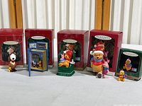 Five Hallmark Keepsake Christmas ornaments displayed in front of their original red boxes, featuring Snoopy and four Pooh themed ornaments.