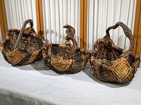 Three large hand woven baskets with grapevine handles displayed side by side on a surface with a white curtain background