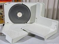 Meat slicer assembled with food carriage and food pusher, blade visible, white textured surfaces.