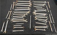 Photo showing a large assortment of wrenches laid out on a black fabric surface, exhibiting varied sizes and signs of surface rust.