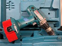 Makita cordless drill with red battery pack inside matching teal carrying case, showing drill details and condition.