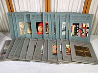 Full view of all 24 volumes laid out on a table, showing two distinct sets with illustrated covers in blue and gray.
