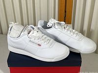 Pair of white Reebok tennis shoes angled showing side, top and overall condition with box underneath