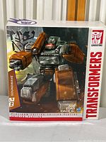 Front of sealed box featuring artwork of Soundwave figure in robot mode with orange and grey colors and Decepticon insignia.