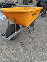 Side angled view of the yellow fiberglass bin and metal frame, showing the black rubber wheel and handle grips.