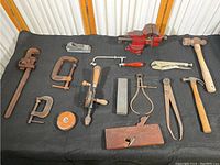 Full view of all tools on black cloth showing variety including bench vise, hand planes, wrenches, hammers, measuring tape and clamps.