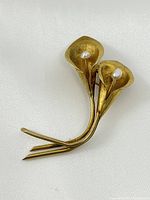 Front angled view of the yellow gold lily flower brooch with two flowers, each centered with a white pearl, on a white background.