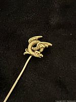 Top angled view of gold dragon stick pin on black background showing full length and dragon figure detail.