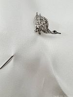 Bird-shaped white gold pin laying on white fabric showing detailed filigree and stones.