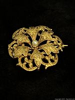 Front view of brooch laid on black background, showing openwork leaf design and central pearl
