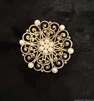 Front view of circular gold filigree brooch with central and outer pearls