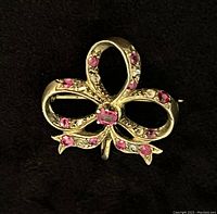 Front view on black background showing full bow-shaped brooch with red rubies and diamond accents.