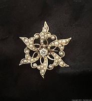 Front view on black background showing starburst design with seed pearls and central diamond.