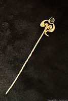 Full length view of the yellow gold stick pin with twisted shaft and decorative top featuring a round green garnet gemstone.