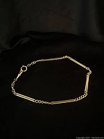 Full view of 11 3/4" 18kt yellow gold chain laid on black fabric, showing alternating bar and round links