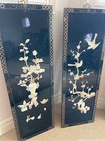 Two Asian style lacquered wood panels standing side by side showing black lacquer finish with floral and bird theme nature collages and decorative geometric borders.