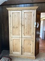Full view of closed pine armoire with two panel doors, showing natural wood finish and rectangular shape.