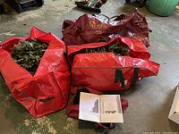Three red storage bags on floor holding unassembled tree branches and instruction manual.