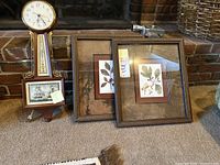 Banjo clock standing next to two framed botanical prints.